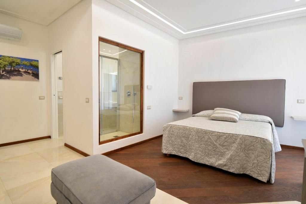 A bedroom with a bed, a bench, a glass door, and a painting on the wall.