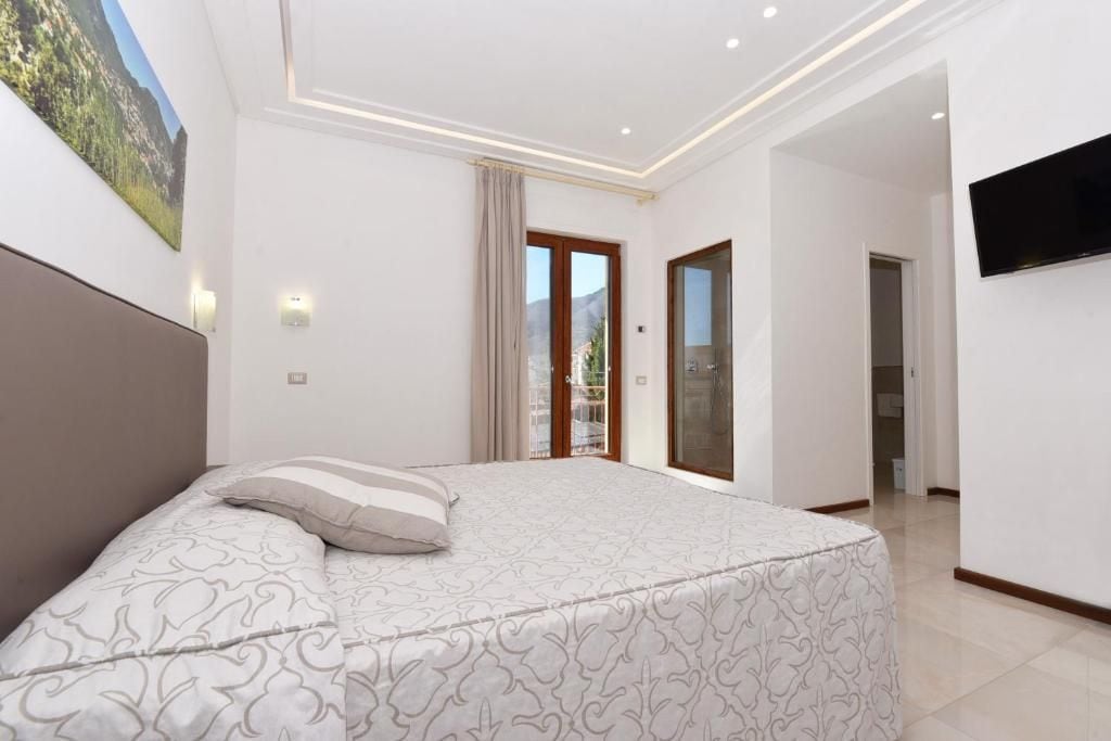 A bedroom with a large bed, a TV mounted on the wall, and a view of the outdoors through a sliding door.