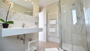 Une salle de bain moderne avec une douche à parois de verre, un lavabo blanc et un mur recouvert de carreaux.
