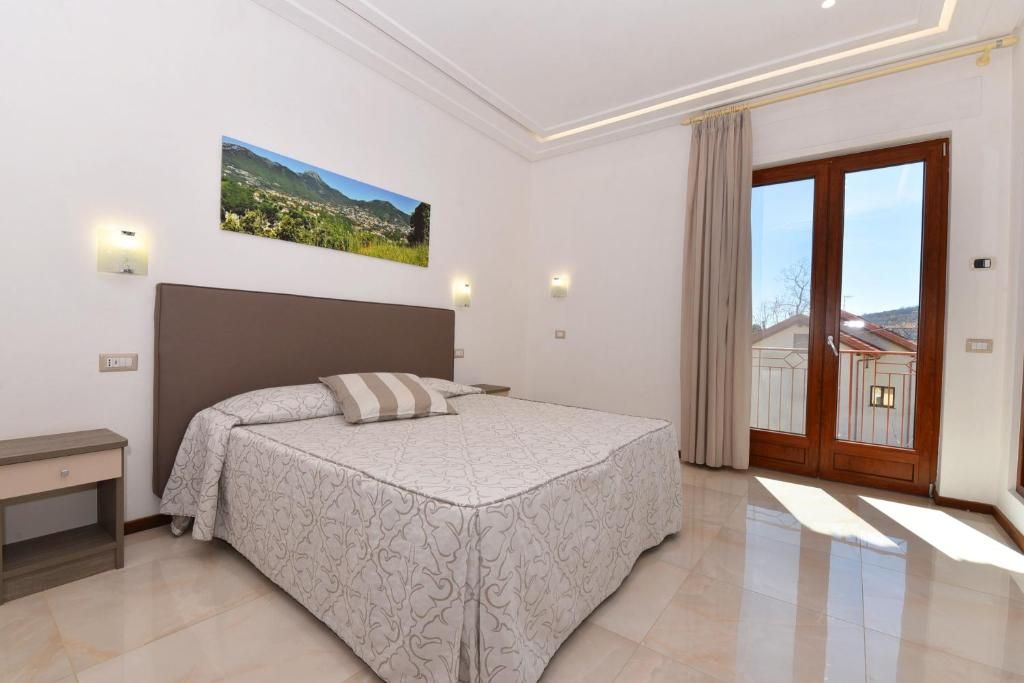 Een slaapkamer met een bed, een nachtkastje, een aan de muur hangend schilderij en een schuifpui naar een balkon.
