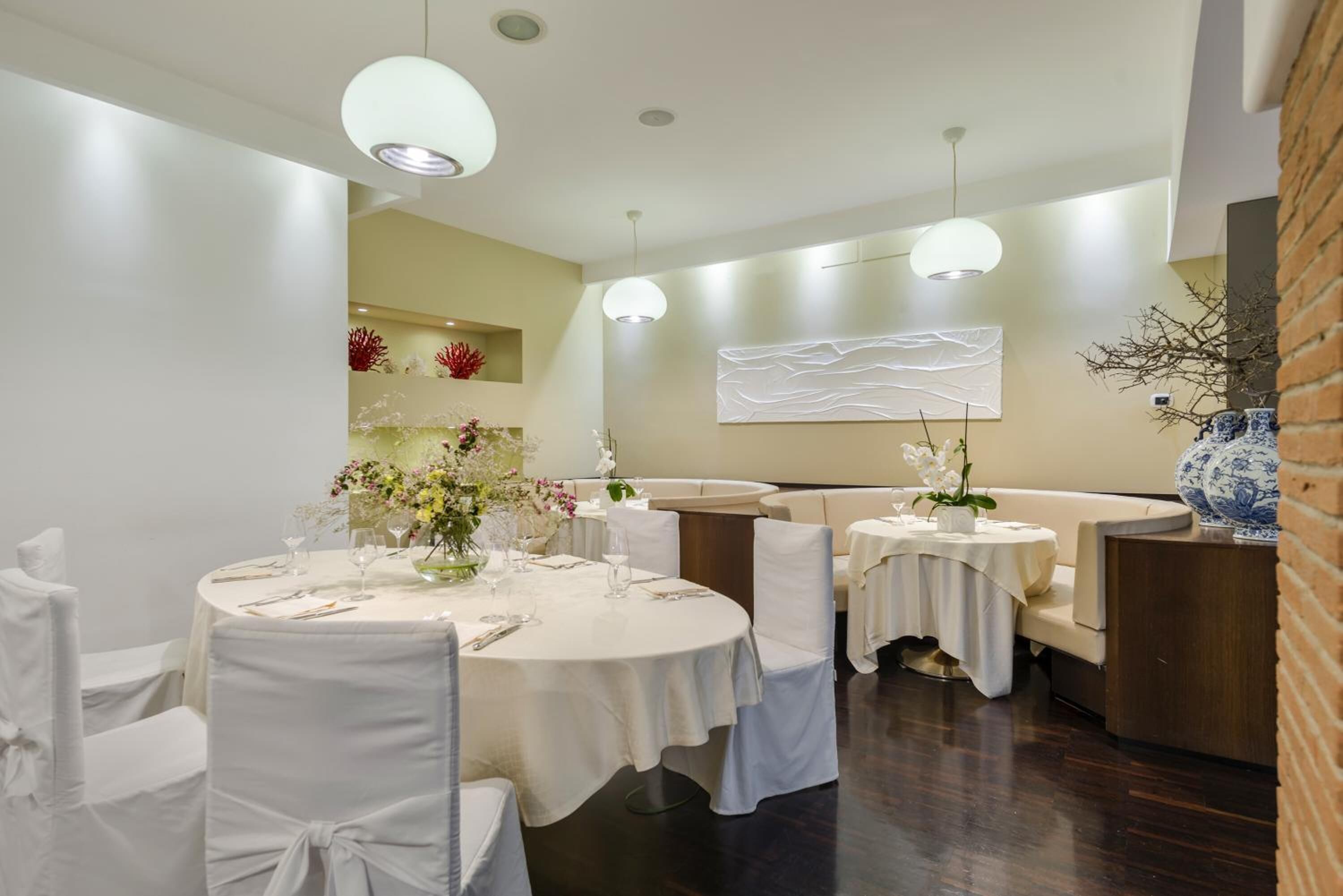 A dining area with round tables, white chairs, and a modern chandelier.
