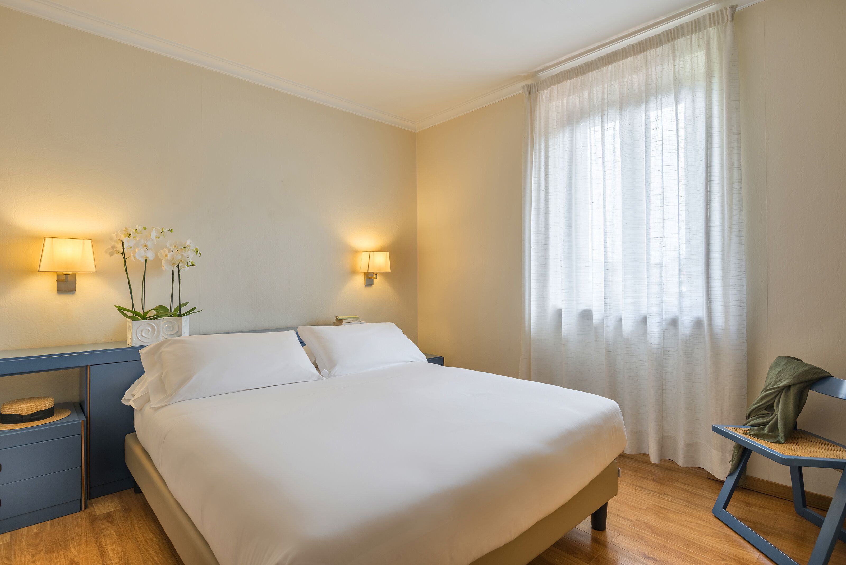 A neatly arranged hotel room with a large bed, bedside lamps, a small table with a plant, and a chair.