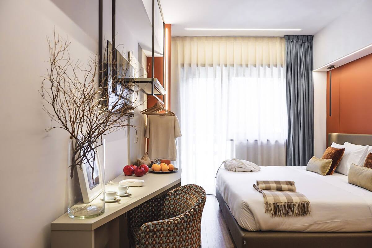 Ein Hotelzimmer mit Bett, Nachttisch, Spiegel und einem Fenster mit Vorhängen.