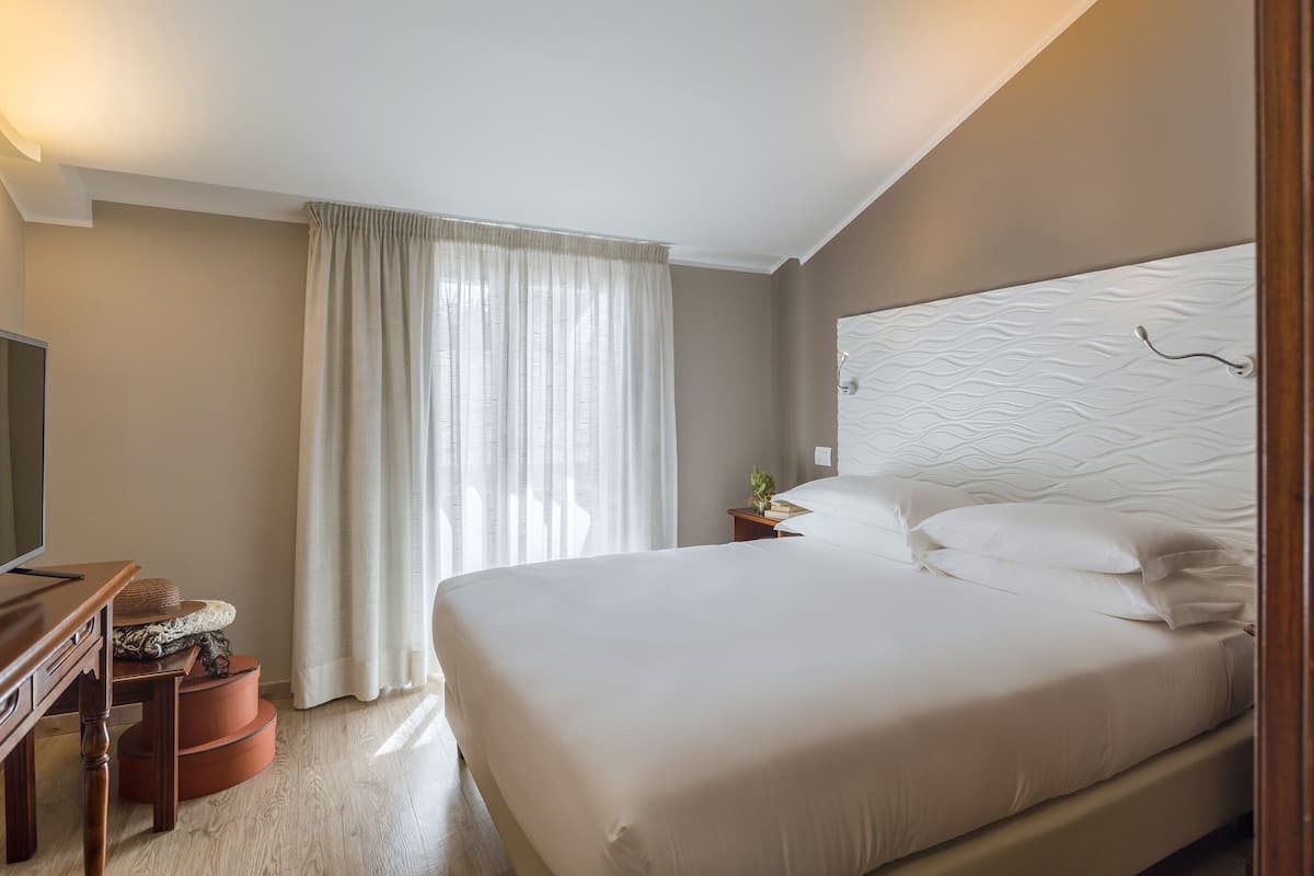Ein ordentlich eingerichtetes Hotelzimmer mit einem großen Bett, einem Fernseher und einem Schreibtisch mit Stuhl.