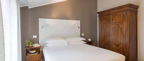 A bedroom with a large bed, wooden nightstand, and a wooden wardrobe.