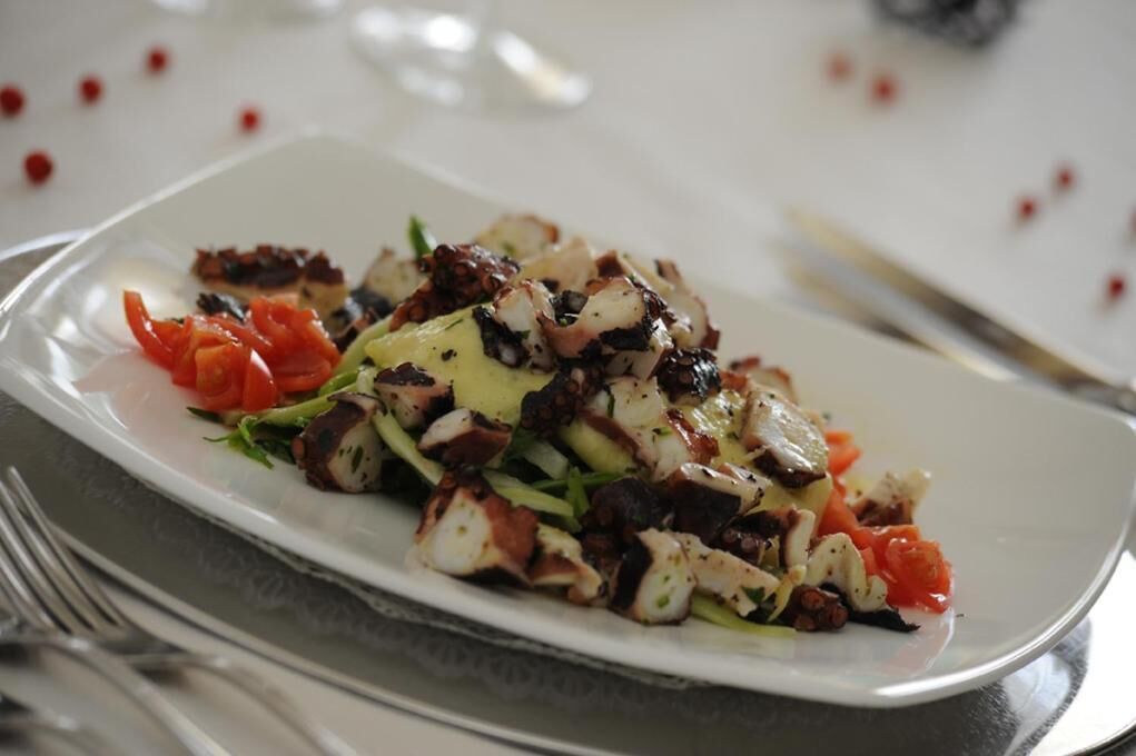 A plated dish with grilled octopus, vegetables, and a drizzle of sauce.