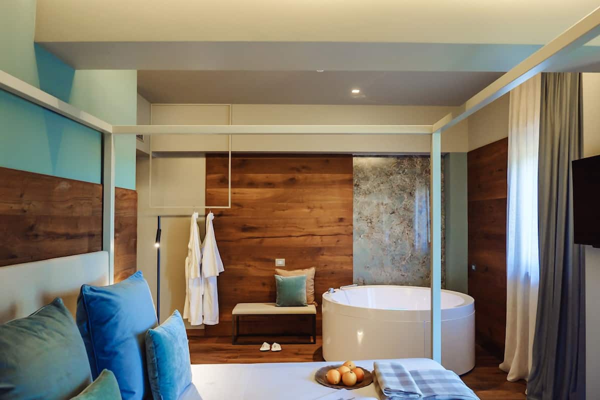 Ein modernes Schlafzimmer mit einem großen Bett, einer Bank, einer Badewanne und Blick ins Badezimmer.