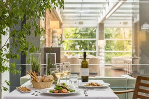 A dining table set with plates, glasses, and a bottle of wine, surrounded by greenery and a glass railing. - Albergo La Pace (Segni)
