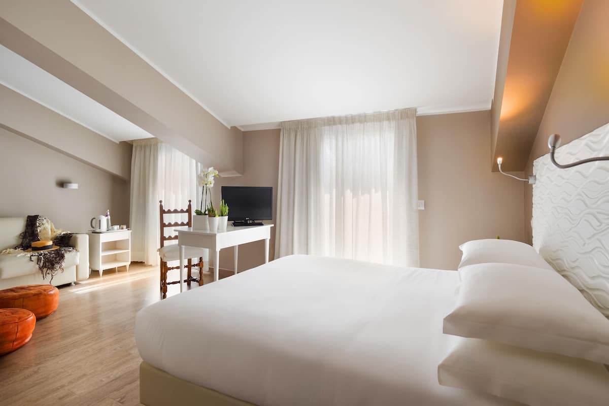 Ein Hotelzimmer mit einem großen Bett, einem Schreibtisch mit Fernseher, einem Sessel und einem kleinen Tisch mit Pflanze.