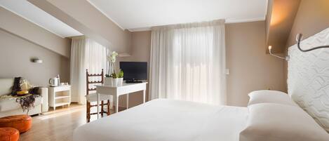 A hotel room with a large bed, a desk with a TV, a chair, and a small table with a plant.