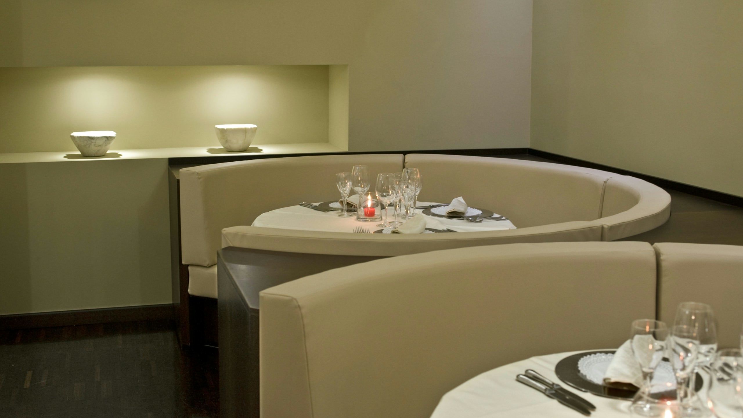 Un comedor moderno con una mesa redonda dispuesta para dos personas, con un candelabro y un florero como centros de mesa.