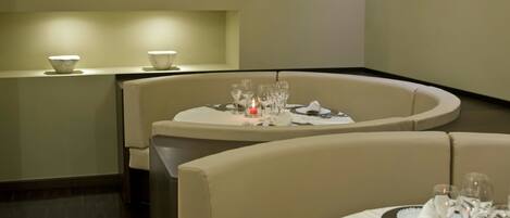 Un comedor moderno con una mesa redonda dispuesta para dos personas, con un candelabro y un florero como centros de mesa.