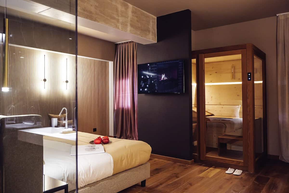 Ein modernes Hotelzimmer mit einem großen Bett, einem eingebauten Fernseher, einem Holzschrank und einer Duschkabine aus Glas.