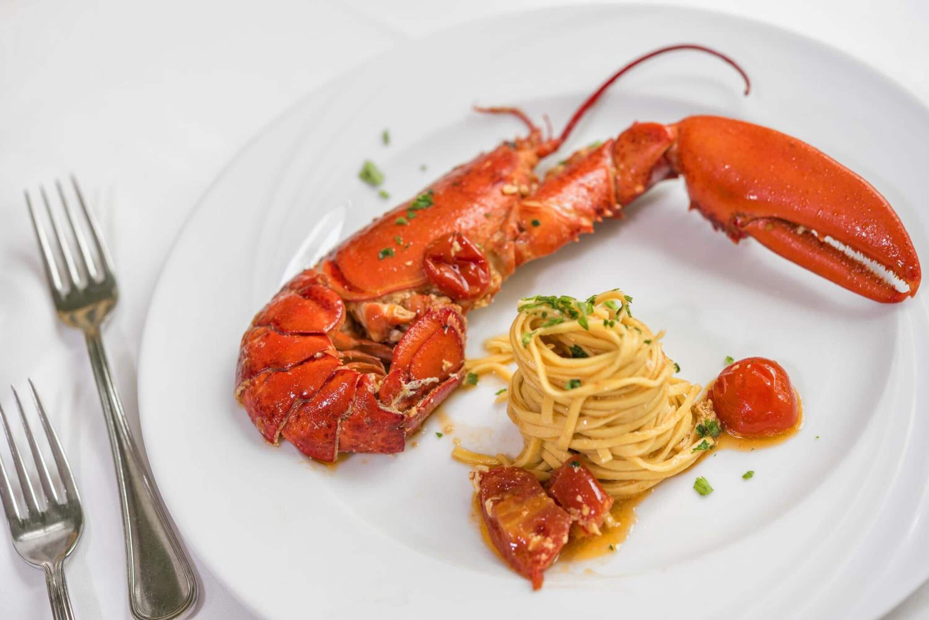 Lagosta com massa e um tomate cereja em um prato branco.