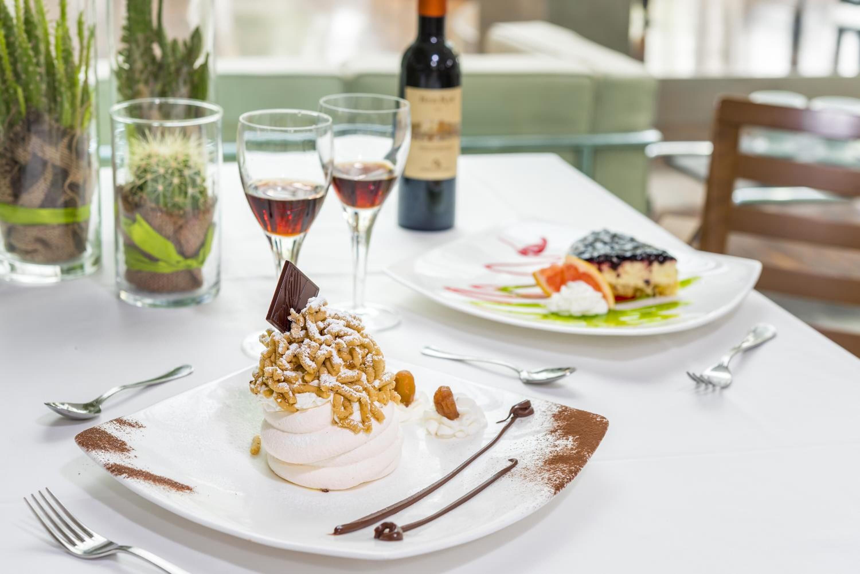 A dessert on a white plate with a fork and spoon beside it, a bottle of wine, and two glasses of red wine on a table.