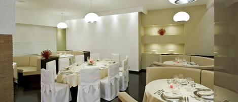 Un comedor moderno con mesas redondas, manteles blancos y sillas cubiertas de blanco.