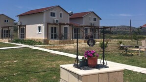 A residential area with houses, a paved walkway, and a stone planter with flowers. - Daphne's Boutique Apartments (Kefalonia)