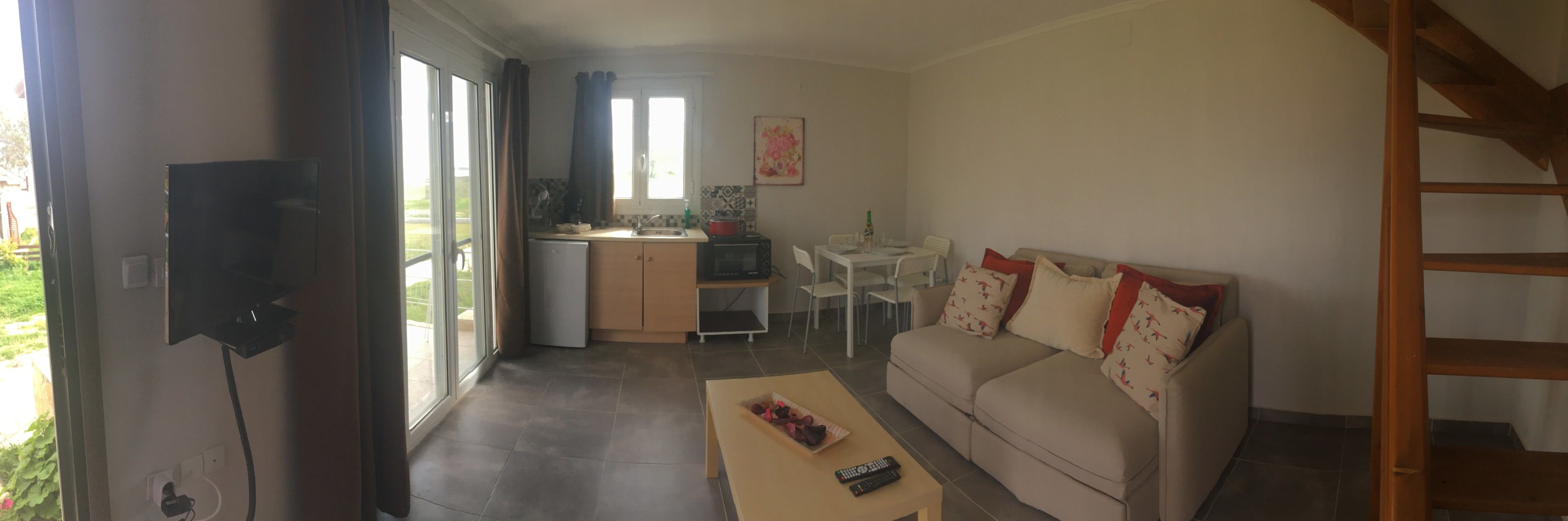 A compact living space with a sofa, a small dining table, a kitchen area, and a TV mounted on the wall.