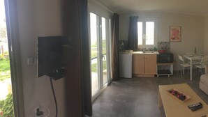 A compact living space with a sofa, a small dining table, a kitchen area, and a TV mounted on the wall. - Daphne's Boutique Apartments (Kefalonia)