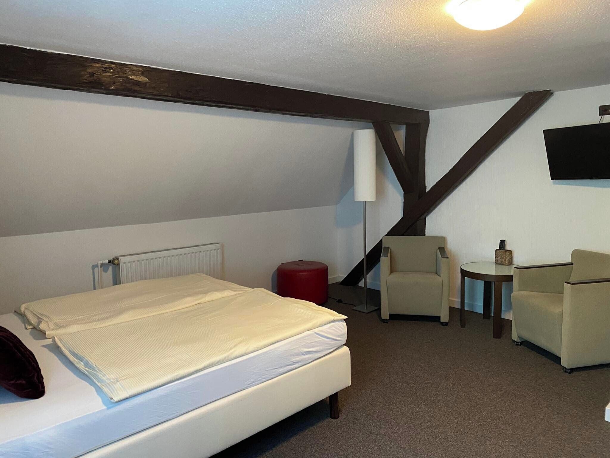 A hotel room with a bed, a chair, a small table, and a television.