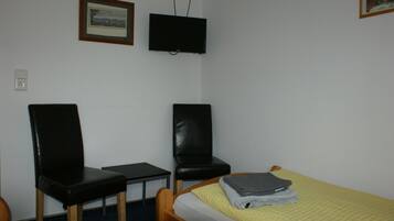 A small room with a bed, two chairs, a desk, a television, and a framed picture on the wall.