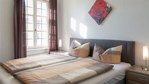Un letto matrimoniale con copripiumino a righe, due cuscini, un comodino con una lampada e una finestra con tende.