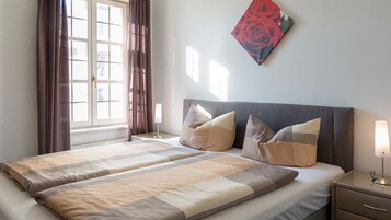 Una cama doble con una colcha a rayas, dos almohadas, una mesita de noche con una lámpara y una ventana con cortinas.