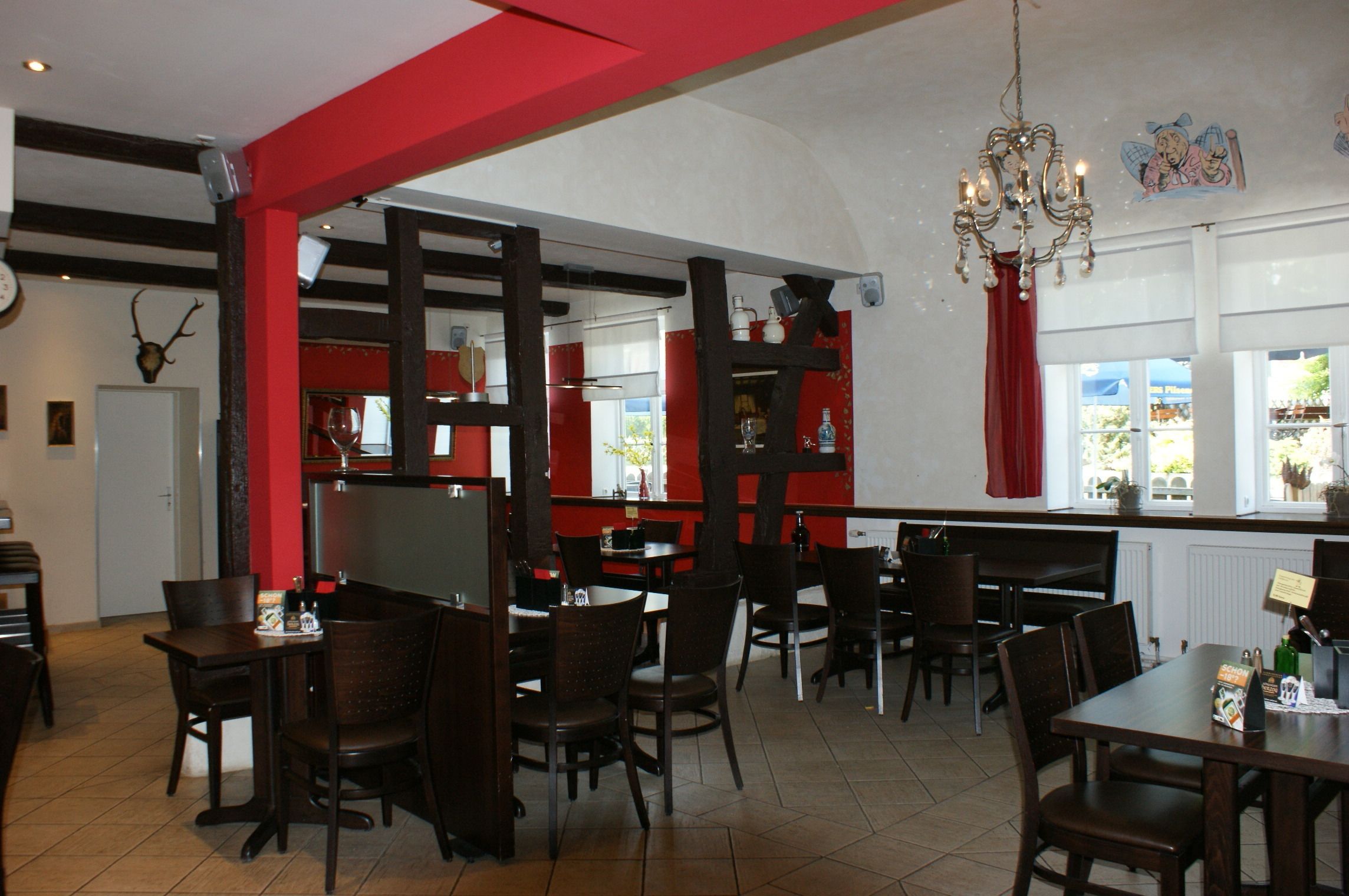 Un restaurante con decoración roja y blanca, muebles de madera y un candelabro.