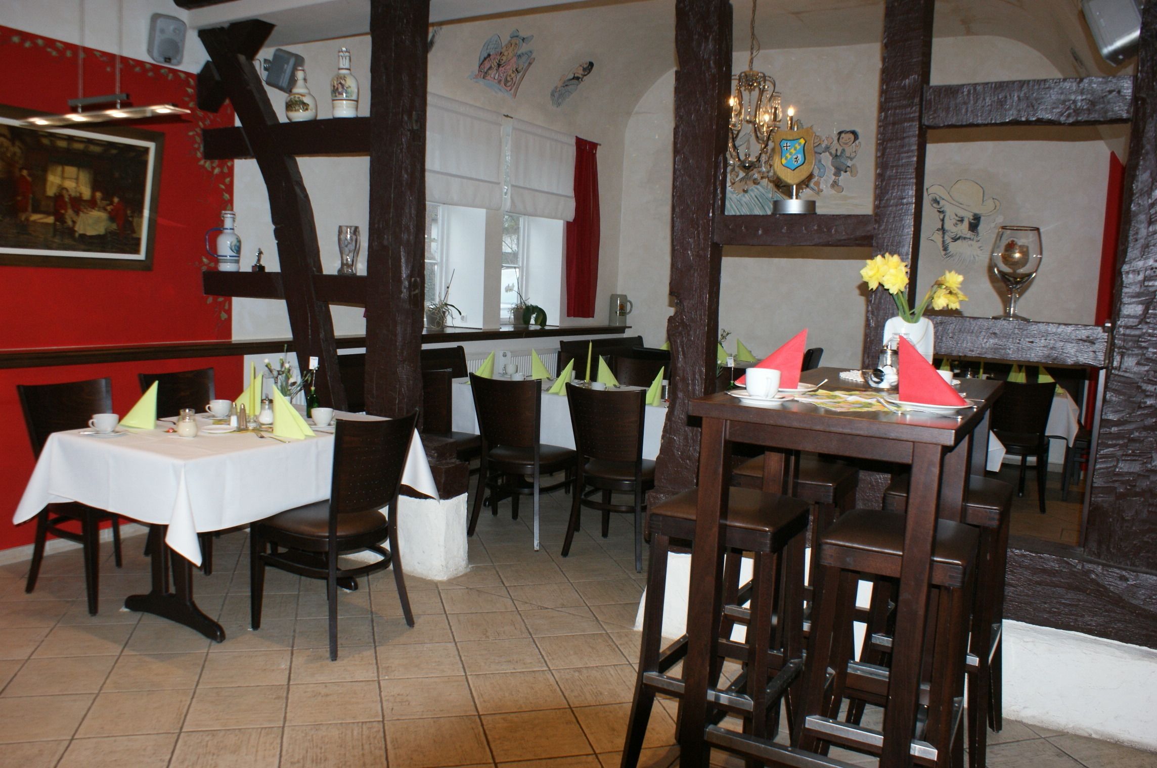 Een restaurant met houten meubels, witte tafelkleden en rode muren.