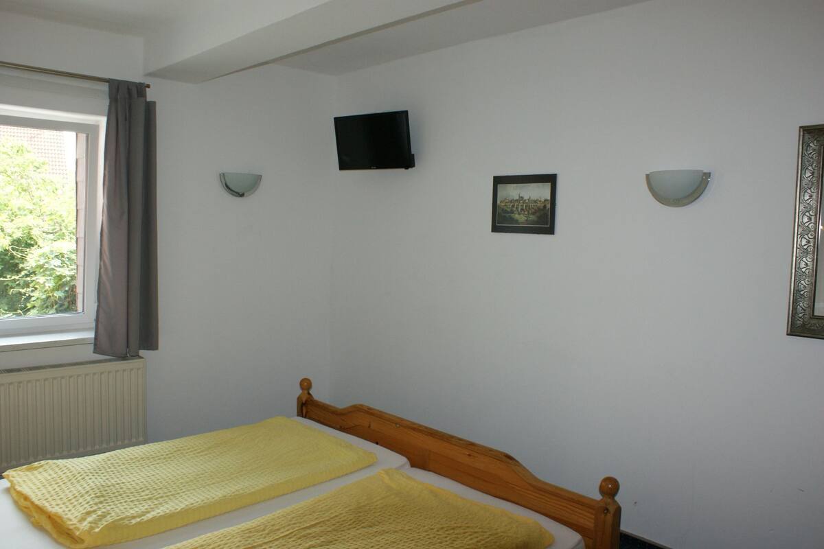 A bedroom with a bed, a window with curtains, a wall-mounted TV, and two wall sconces.
