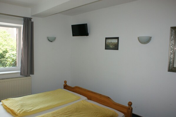 A bedroom with a bed, a window with curtains, a wall-mounted TV, and two wall sconces.