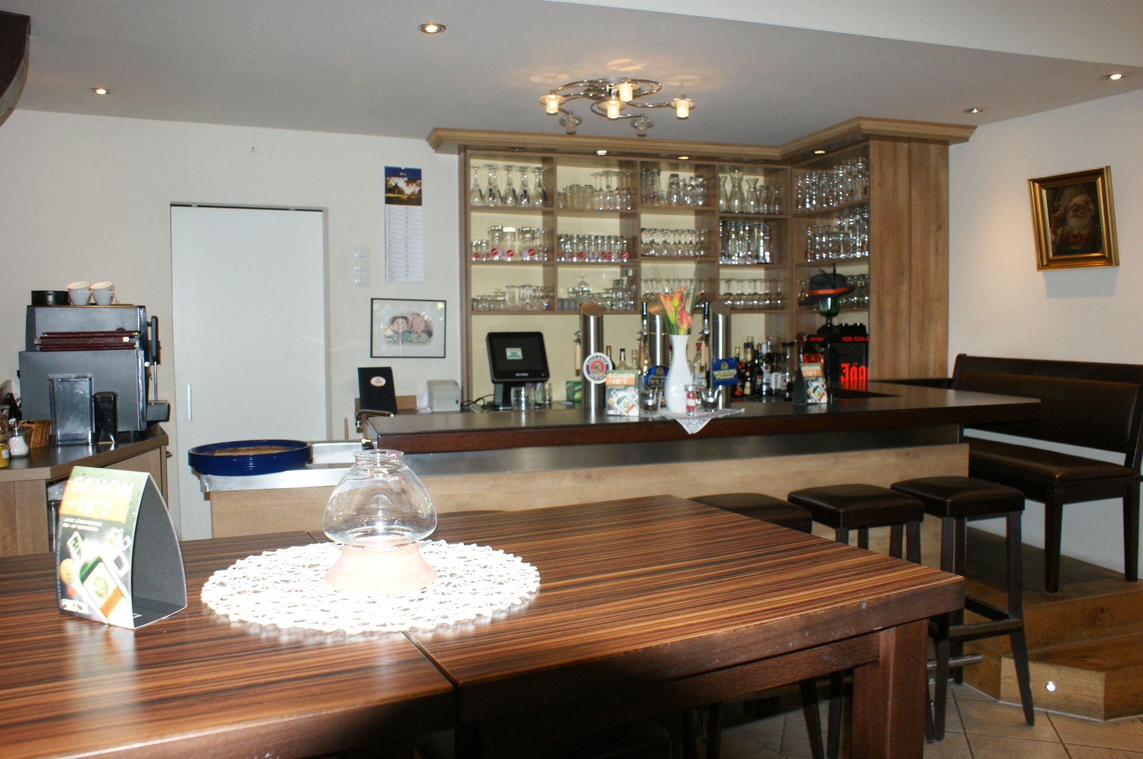 Zona de bar con mostrador de madera, taburetes y una exhibición de cristalería.
