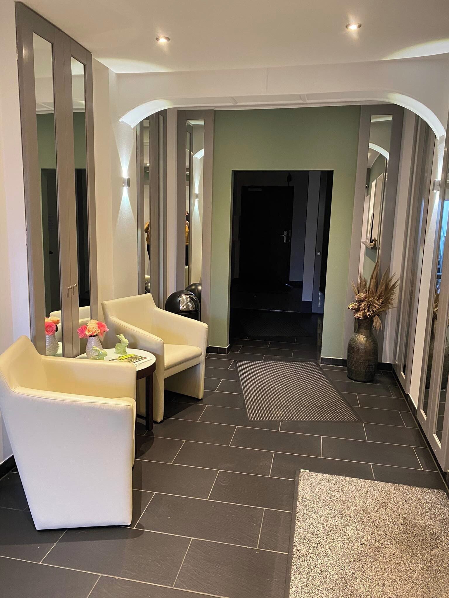 A modern hotel lobby with a seating area, a reception desk, and a hallway leading to the rooms.
