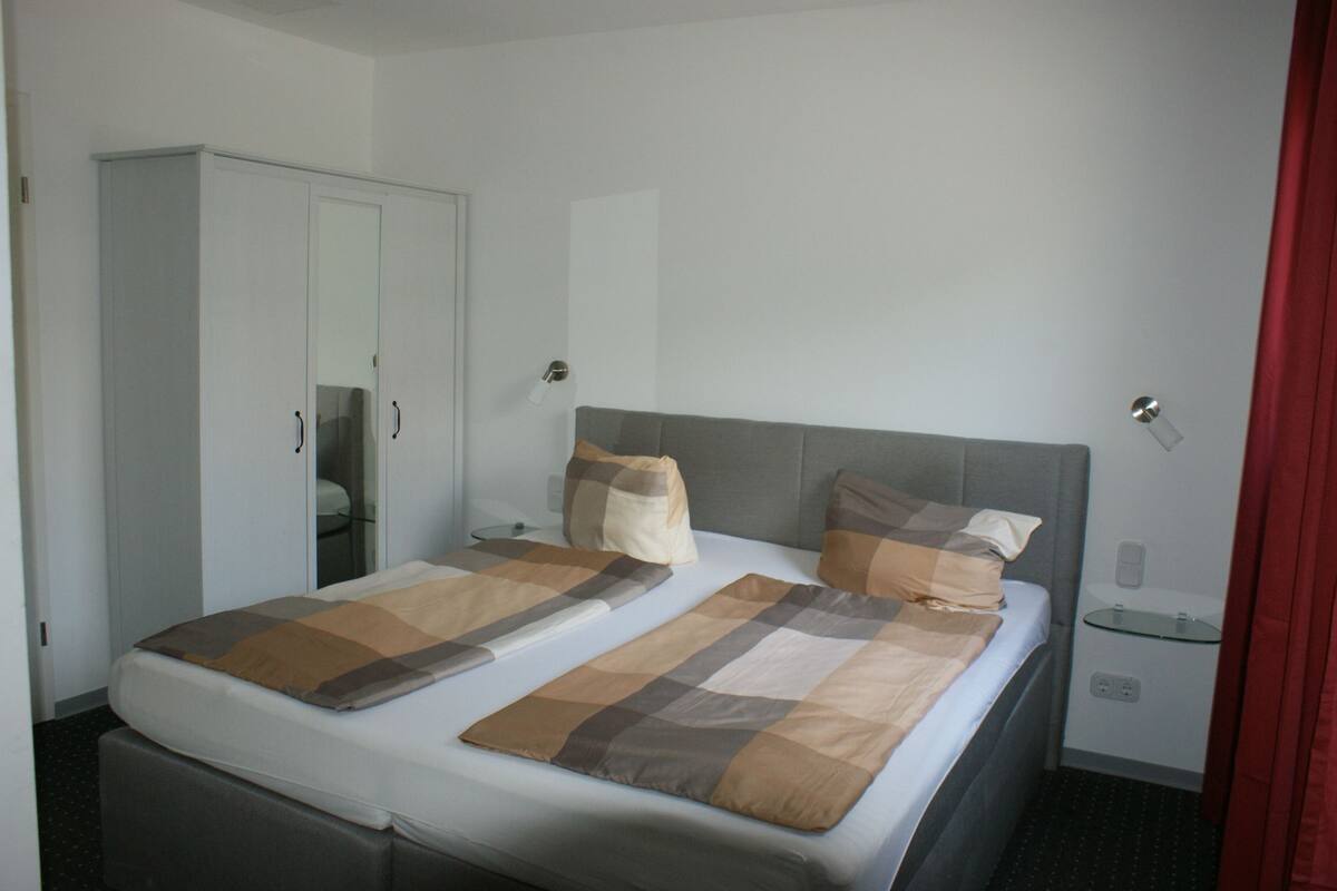 A hotel room with a bed, a wardrobe, a bedside table, and a mirror.