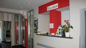 Una reception con arredamento rosso e bianco, una parete divisoria in vetro e un vaso con una pianta.