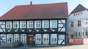 Un edificio tradizionale a struttura in legno e riempimento in mattoni, con tetto in tegole rosse, un ingresso ben visibile con la scritta "FORSTHAUS" e un cartello pubblicitario per un "Brunchbuffet".