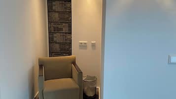 A hallway with a beige armchair, a bookshelf, and a wall-mounted light fixture.