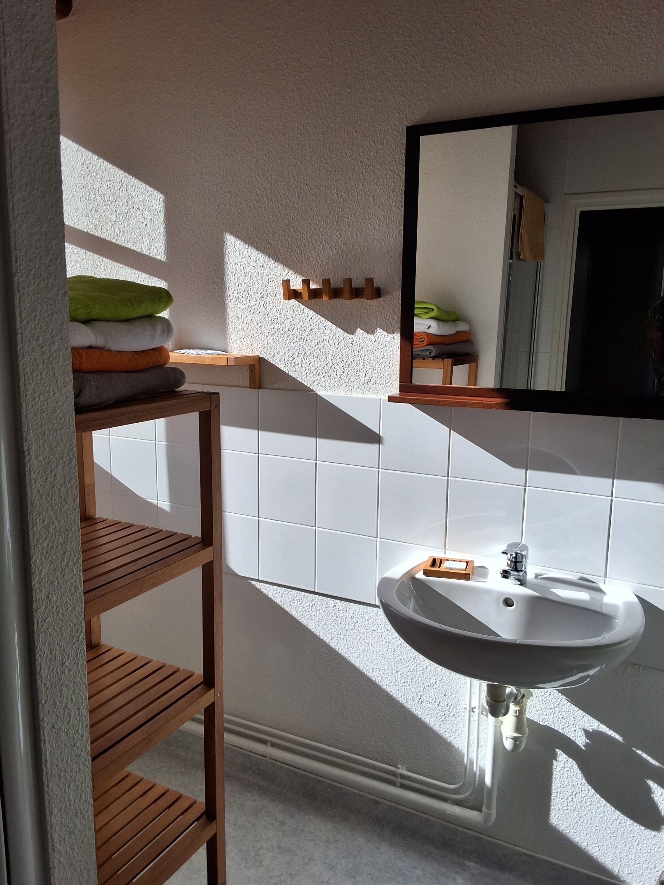 A bathroom with a white sink, wooden shelves, a mirror, and a towel rack.
