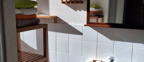 Casa de banho com lavatório branco, prateleiras de madeira, espelho e porta-toalhas.