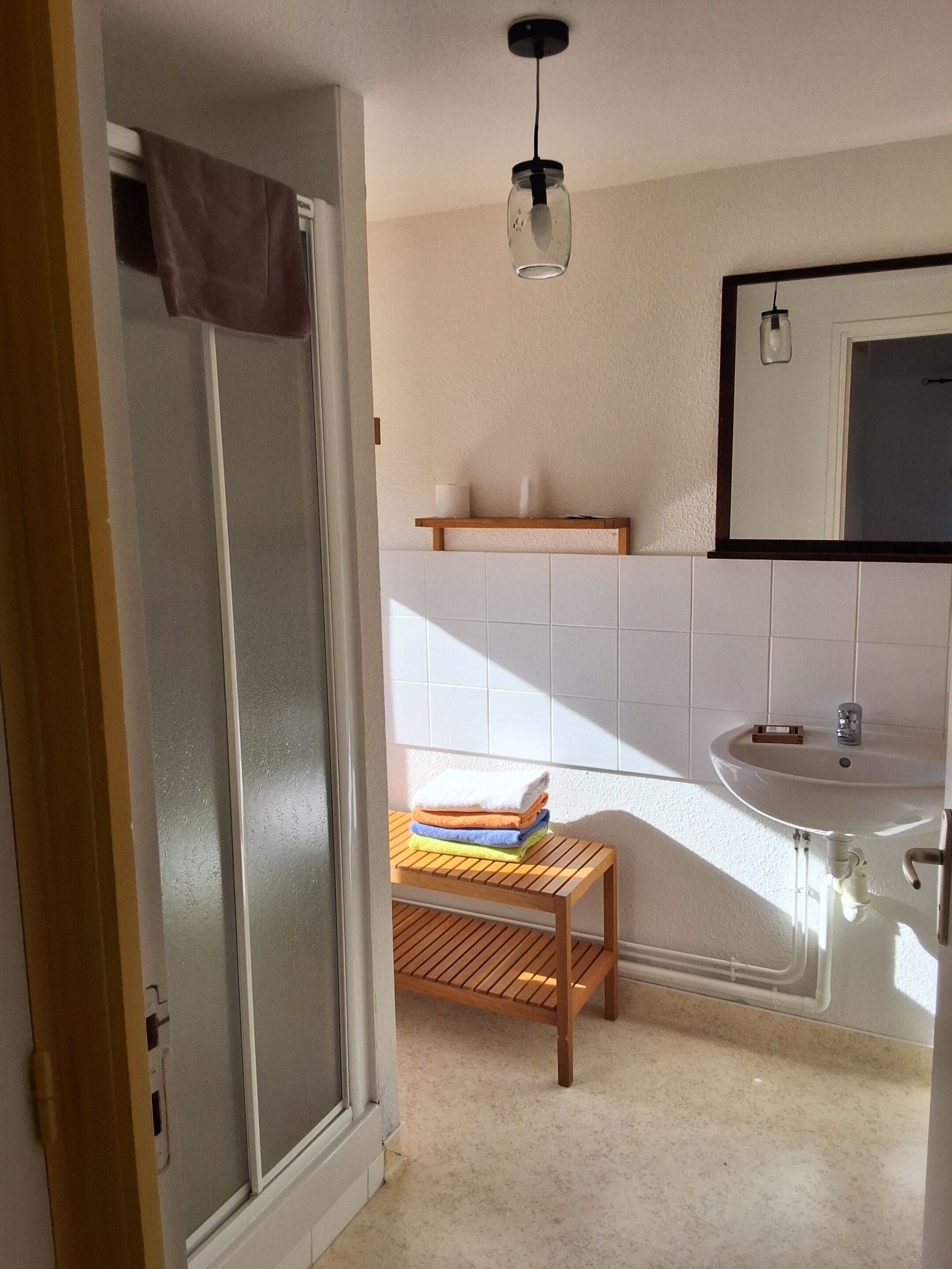 Un bagno con doccia, lavandino e mensola in legno.