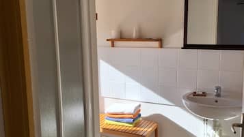 A bathroom with a shower, a sink, and a wooden shelf.