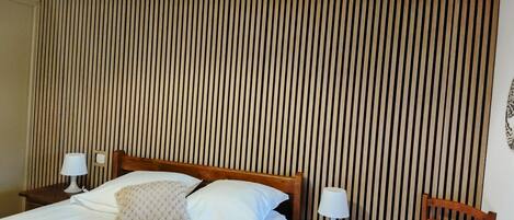 Un dormitorio con una cama, dos mesitas de noche, una silla y un revestimiento de listones de madera.