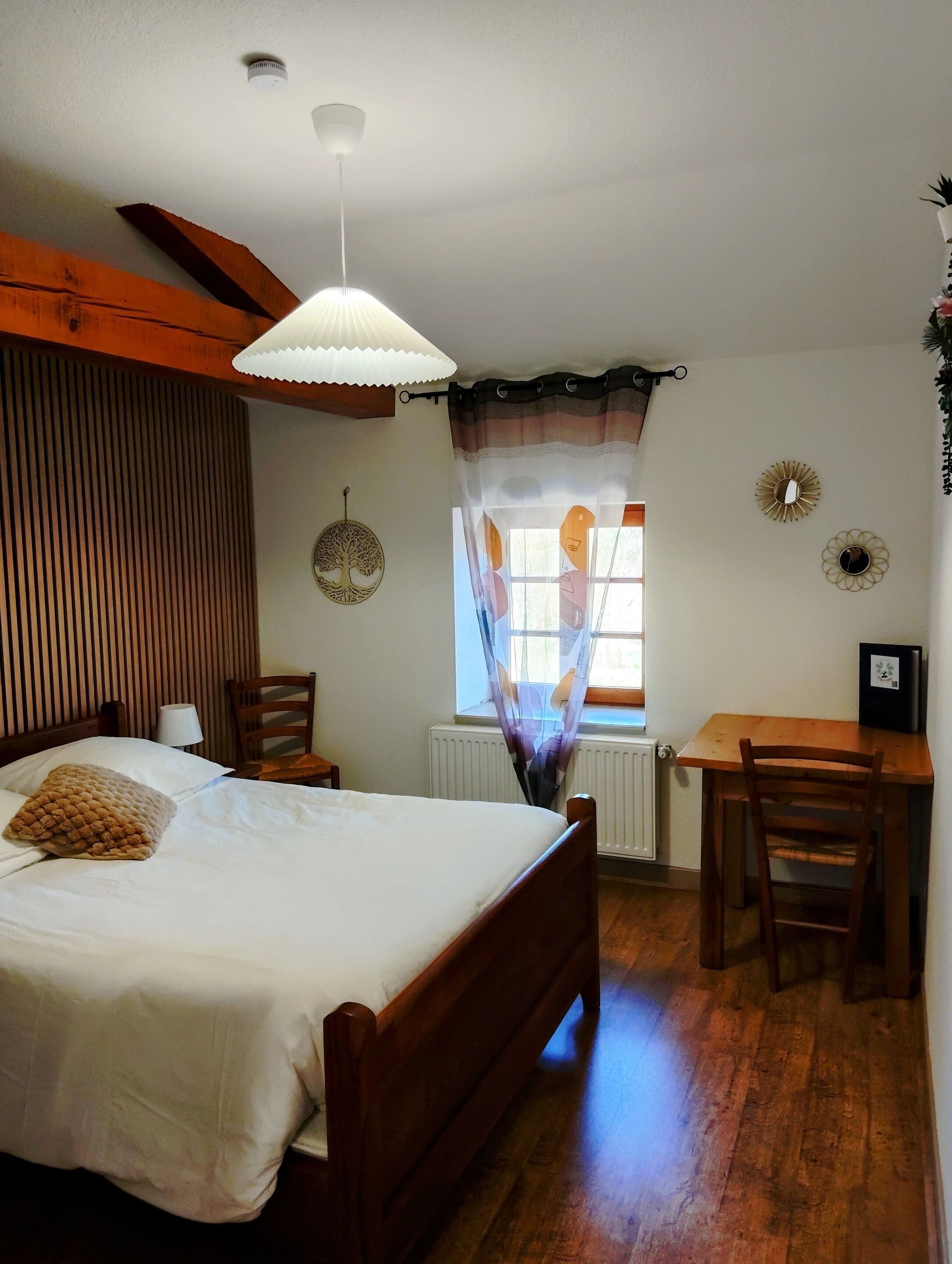 A bedroom with a bed, a desk, a chair, a window with curtains, a radiator, and a ceiling fan.