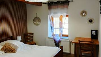 A bedroom with a bed, a desk, a chair, a window with curtains, a radiator, and a ceiling fan.