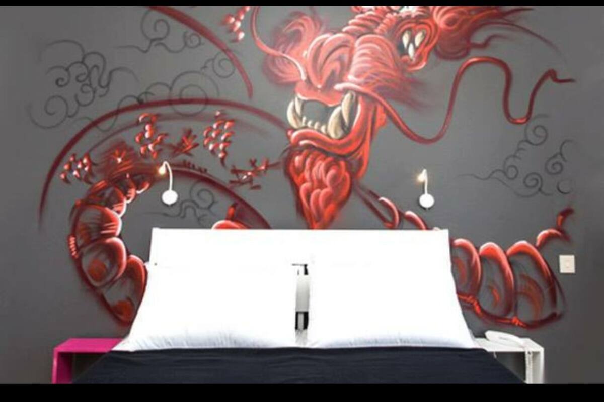 A bedroom with a bed, a nightstand, and a wall mural of a red dragon.