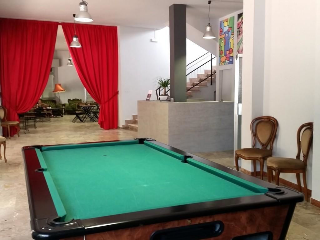 Ein Billardtisch in einem Raum mit roten Vorhängen, einer Treppe und einem Essbereich.