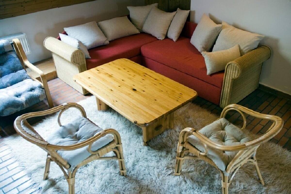 A cozy living room with a red sofa, two wicker chairs, a wooden coffee table, and a fluffy rug.