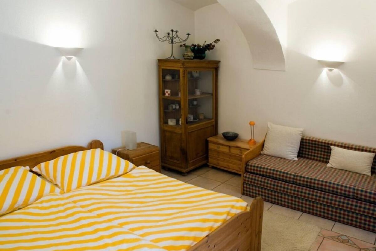 A bedroom with a bed, a wooden cabinet, a sofa, and two wall-mounted lights.