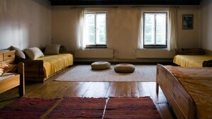 A room with two beds, a wooden floor, a red rug, and two windows with curtains. - Růžová chalupa u Šimánků (Rtyne v Podkrkonosí)