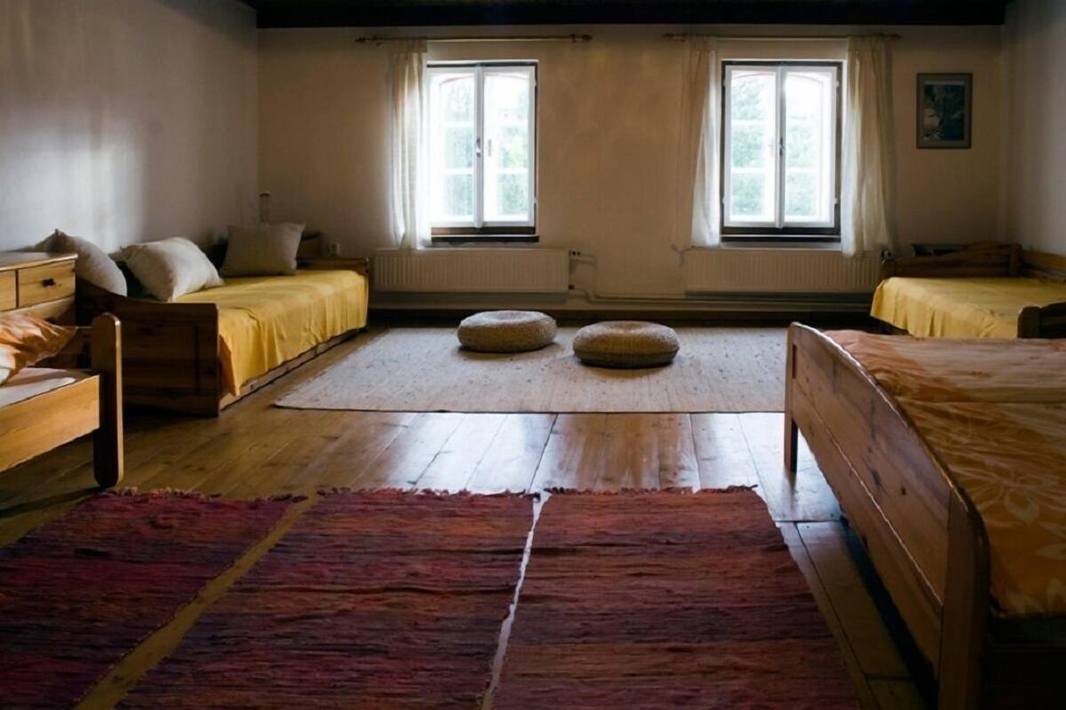 A room with two beds, a wooden floor, a red rug, and two windows with curtains.